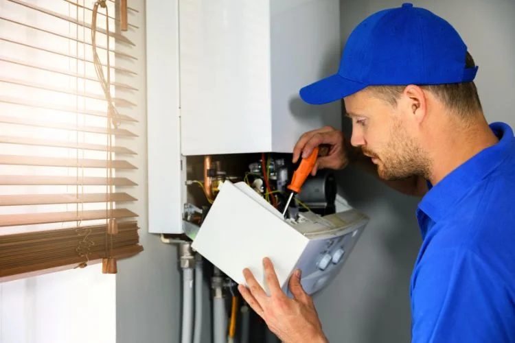 Un technicien en tenue bleu qui répare une chaudière défectueuse.