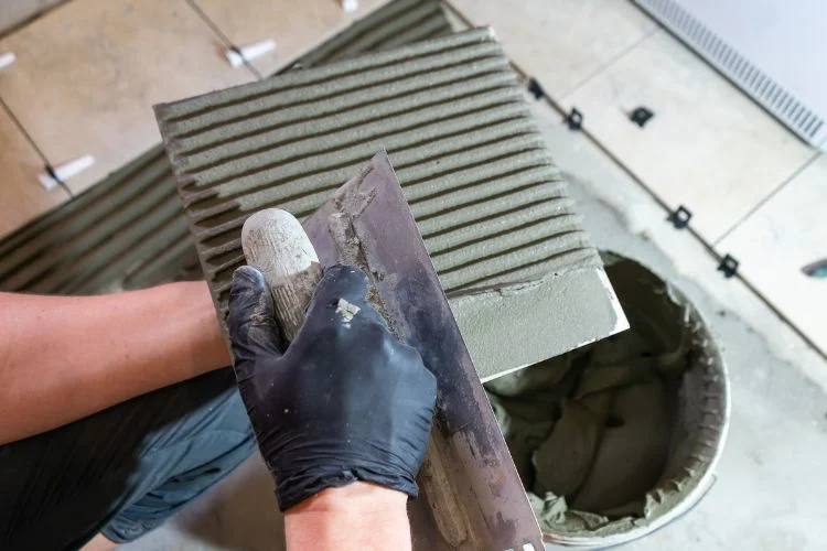 Un artisan qui pose du mortier-colle sur du carrelage.