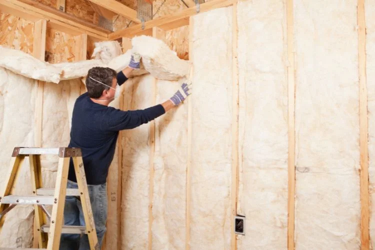 Un homme qui pose une couche de laine de verre pour l'isolation sur un mur.