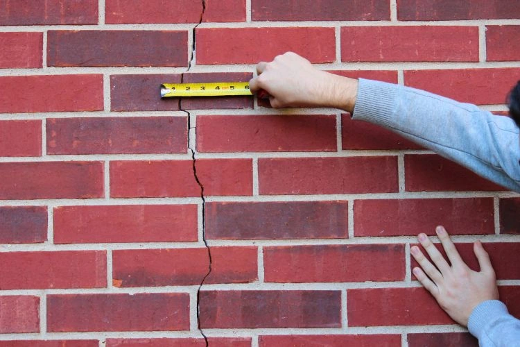 Personne en train de prendre des mesures sur une fissure de mur extérieur